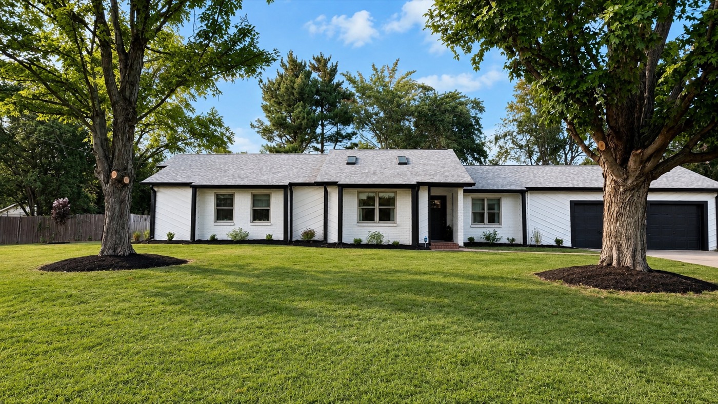Front of the house — white painted brick ranch with black trim, two big shade trees in the lawn