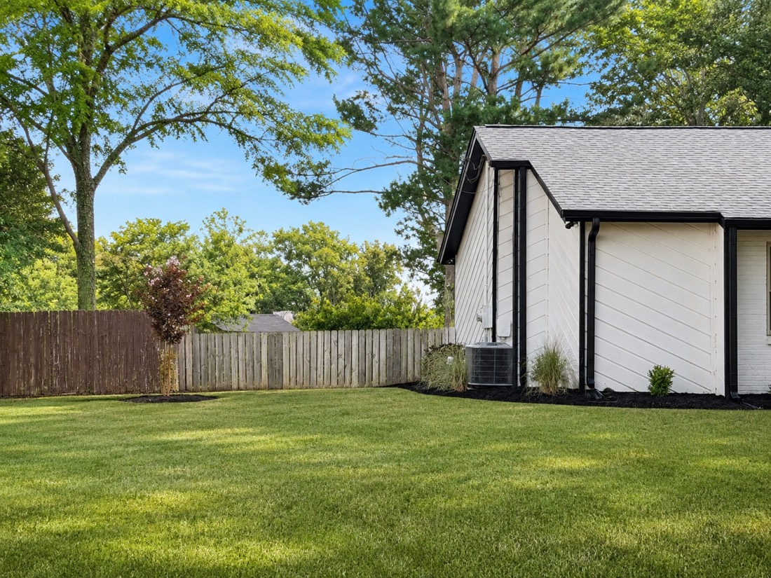 Left side of the backyard with crape myrtle by the fence and muhly grass near the AC unit